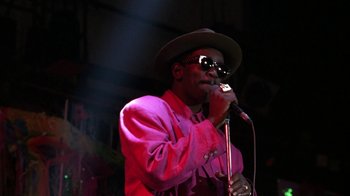 Movie still from “New Jack City” (1991), directed by Mario Van Peebles – A man in a hat and sunglasses singing into a microphone; Close Up shot, Low angle