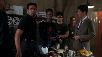 Movie still from “New Jack City” (1991), directed by Mario Van Peebles – A group of men standing next to each other in a room; Medium shot, Over the shoulder angle
