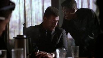 Movie still from “New Jack City” (1991), directed by Mario Van Peebles – A man sitting at a table with another man looking at him; Close Up shot, Low angle