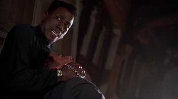 Movie still from “New Jack City” (1991), directed by Mario Van Peebles – A man holding onto a chain while sitting on a chair; Close Up shot, Low angle