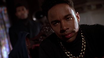 Movie still from “New Jack City” (1991), directed by Mario Van Peebles – A person wearing a chain around their neck; Close Up shot, Over the shoulder angle