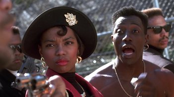 Movie still from “New Jack City” (1991), directed by Mario Van Peebles – A man and a woman standing next to each other in front of a chain link fence; Close Up shot, Low angle