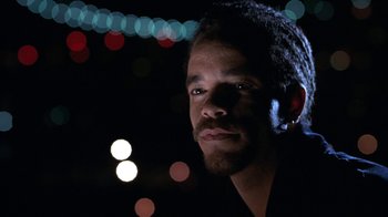 Movie still from “New Jack City” (1991), directed by Mario Van Peebles – A person wearing a black shirt with lights in the background; Close Up shot, Low angle
