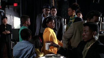 Movie still from “New Jack City” (1991), directed by Mario Van Peebles – A group of people standing around a table with drinks; Medium shot, Over the shoulder angle