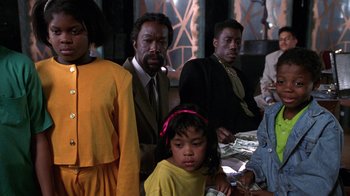 Movie still from “New Jack City” (1991), directed by Mario Van Peebles – A group of people standing next to each other in a room; Medium shot, Over the shoulder angle