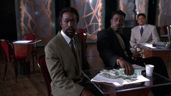 Movie still from “New Jack City” (1991), directed by Mario Van Peebles – Two men sitting at a table with money in front of them; Medium shot, Low angle