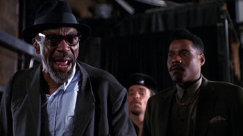 Movie still from “New Jack City” (1991), directed by Mario Van Peebles – A group of men standing next to each other in a room; Close Up shot, Low angle