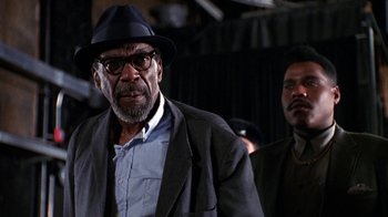 Movie still from “New Jack City” (1991), directed by Mario Van Peebles – An older man wearing a hat and glasses; Close Up shot, Low angle