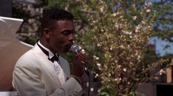 Movie still from “New Jack City” (1991), directed by Mario Van Peebles – A man in a white suit is singing into a microphone; Close Up shot, High angle