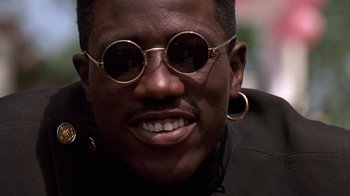 Movie still from “New Jack City” (1991), directed by Mario Van Peebles – A person wearing glasses and smiling; Close Up shot, Low angle