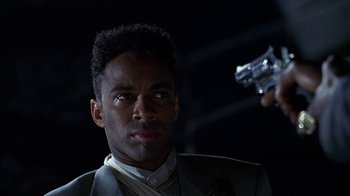 Movie still from “New Jack City” (1991), directed by Mario Van Peebles – A man holding a gun while standing next to another man; Close Up shot, Low angle