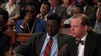 Movie still from “New Jack City” (1991), directed by Mario Van Peebles – A group of people sitting in a room; Medium shot, Over the shoulder angle