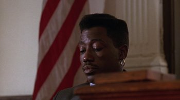 Movie still from “New Jack City” (1991), directed by Mario Van Peebles – A person sitting in front of an american flag; Close Up shot, Low angle