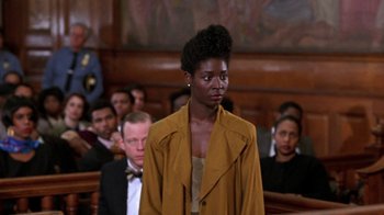 Movie still from “New Jack City” (1991), directed by Mario Van Peebles – A woman standing in front of a group of people in a court room; Medium shot, Over the shoulder angle