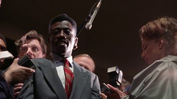 Movie still from “New Jack City” (1991), directed by Mario Van Peebles – A man wearing a suit and tie holding a microphone; Close Up shot, Low angle
