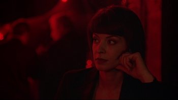 Movie still from “New Rose Hotel” (1998), directed by Abel Ferrara – A woman in a black jacket is sitting in a dark room; Close Up shot, Low angle