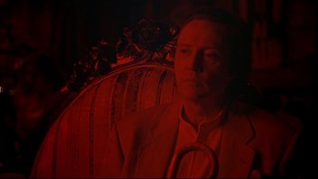 Movie still from “New Rose Hotel” (1998), directed by Abel Ferrara – A man in a suit and tie sitting in a chair; Close Up shot, Low angle