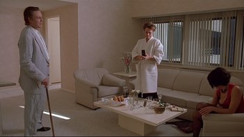 Movie still from “New Rose Hotel” (1998), directed by Abel Ferrara – A woman in a white bathrobe standing in a living room; Wide shot, High angle