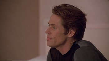 Movie still from “New Rose Hotel” (1998), directed by Abel Ferrara – A person wearing a black shirt looking to the side; Close Up shot, Over the shoulder angle