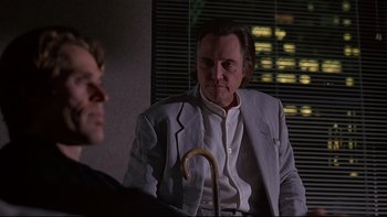 Movie still from “New Rose Hotel” (1998), directed by Abel Ferrara – A man in a white jacket holding an umbrella; Medium shot, Over the shoulder angle