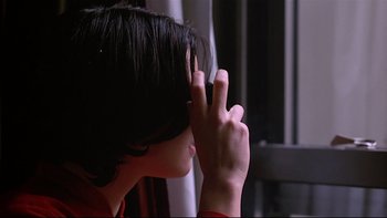 Movie still from “New Rose Hotel” (1998), directed by Abel Ferrara – A person with their hand up to their face; Close Up shot, Over the shoulder angle