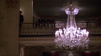 Movie still from “New Rose Hotel” (1998), directed by Abel Ferrara – A chandelier in the middle of a room with a railing in the background; Wide shot, Low angle