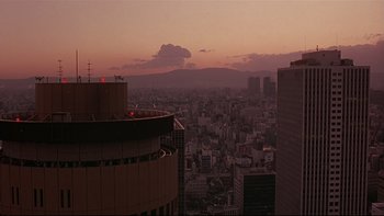 Movie still from “New Rose Hotel” (1998), directed by Abel Ferrara – A view of a city skyline at sunset; Extreme Wide shot, Low angle