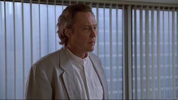 Movie still from “New Rose Hotel” (1998), directed by Abel Ferrara – A man in a white shirt and a white jacket looking to his left; Close Up shot, Low angle