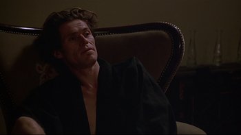 Movie still from “New Rose Hotel” (1998), directed by Abel Ferrara – A man sitting in a chair wearing a black robe; Close Up shot, Low angle