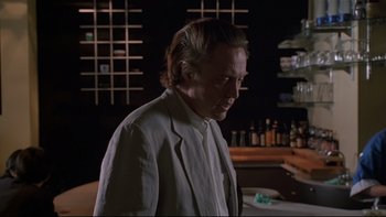 Movie still from “New Rose Hotel” (1998), directed by Abel Ferrara – A man standing in front of a counter in a room; Close Up shot, Low angle