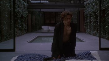 Movie still from “New Rose Hotel” (1998), directed by Abel Ferrara – A shirtless man kneeling down in front of a swimming pool; Medium shot, Over the shoulder angle