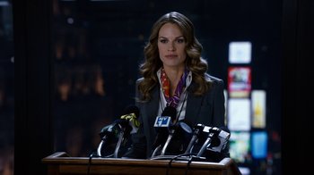 Movie still from “New Year's Eve” (2011), directed by Garry Marshall – A woman standing at a podium with microphones in front of her; Medium shot, Over the shoulder angle