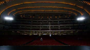 Movie still from “New Year's Eve” (2011), directed by Garry Marshall – A man standing in an empty theater with a microphone; Extreme Wide shot, High angle