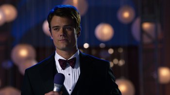 Movie still from “New Year's Eve” (2011), directed by Garry Marshall – A man in a tuxedo holding a microphone and wearing a bow tie; Close Up shot, Over the shoulder angle