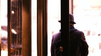 Movie still from “New York, I Love You” (2008), directed by Wen Jiang – A man wearing a hat standing in front of a window; Medium shot, Over the shoulder angle