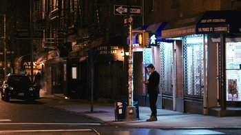 Movie still from “New York, I Love You” (2008), directed by Wen Jiang – A man standing on a street corner looking at his cell phone; Wide shot, High angle