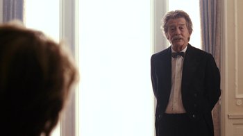 Movie still from “New York, I Love You” (2008), directed by Wen Jiang – An older man in a tuxedo standing in front of a window; Medium shot, Over the shoulder angle