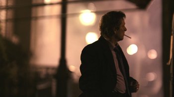 Movie still from “New York, I Love You” (2008), directed by Wen Jiang – A man smoking a cigarette while wearing a suit and tie; Medium shot, Over the shoulder angle