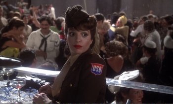 Movie still from “New York, New York” (1977), directed by Martin Scorsese – A woman in a military uniform is standing in front of a group of people; Medium shot, Over the shoulder angle