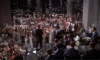 Movie still from “New York, New York” (1977), directed by Martin Scorsese – A large crowd of people are gathered in a large room; Extreme Wide shot, High angle