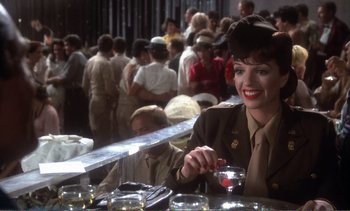 Movie still from “New York, New York” (1977), directed by Martin Scorsese – A woman sitting at a table in front of a group of people; Medium shot, Over the shoulder angle
