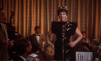 Movie still from “New York, New York” (1977), directed by Martin Scorsese – A woman standing at a microphone in front of a group of people; Medium shot, Over the shoulder angle