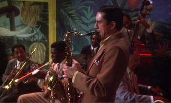 Movie still from “New York, New York” (1977), directed by Martin Scorsese – A man playing a saxophone in front of a group of other men; Medium shot, Low angle