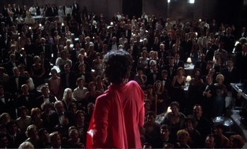 Movie still from “New York, New York” (1977), directed by Martin Scorsese – A crowd of people sitting and standing in front of a woman; Extreme Wide shot, High angle
