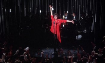 Movie still from “New York, New York” (1977), directed by Martin Scorsese – A woman in a red jacket is on a microphone; Wide shot, High angle