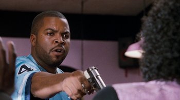 Movie still from “Next Friday” (2000), directed by Steve Carr – A man holding a gun while sitting in a room; Close Up shot, Over the shoulder angle