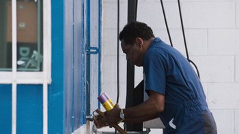 Movie still from “Next Friday” (2000), directed by Steve Carr – A man is holding a paint brush while standing in front of a blue wall; Medium shot, Low angle