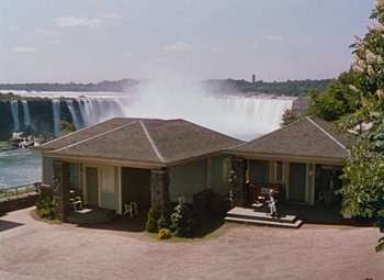 Movie still from “Niagara” (1953), directed by Henry Hathaway – A man on a motorcycle rides past a house with a waterfall in the background; Extreme Wide shot, High angle