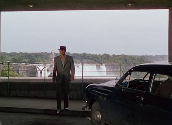Movie still from “Niagara” (1953), directed by Henry Hathaway – A man standing next to a car near a body of water; Wide shot, Over the shoulder angle