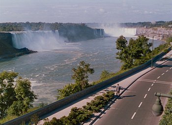Movie still from “Niagara” (1953), directed by Henry Hathaway – A man riding a bike down the side of a road near a waterfall; Extreme Wide shot, High angle